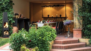 Een terras buiten met een bakstenen muur, een vuurplaats en een eettafel.