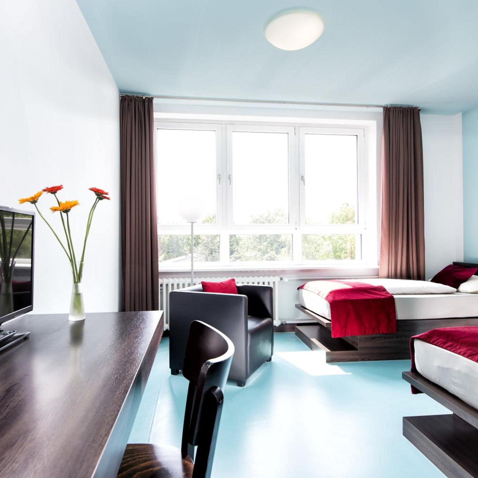 Une chambre d’hôtel avec un lit, un bureau, une chaise et une fenêtre avec des rideaux.