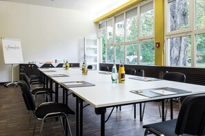 A conference room with a long table, chairs, a whiteboard, and large windows with a view of trees. - TOP Embrace Hotel Grenzfal (Berlin)