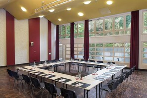 Una sala de conferencias con una mesa larga, sillas y ventanas amplias con cortinas.