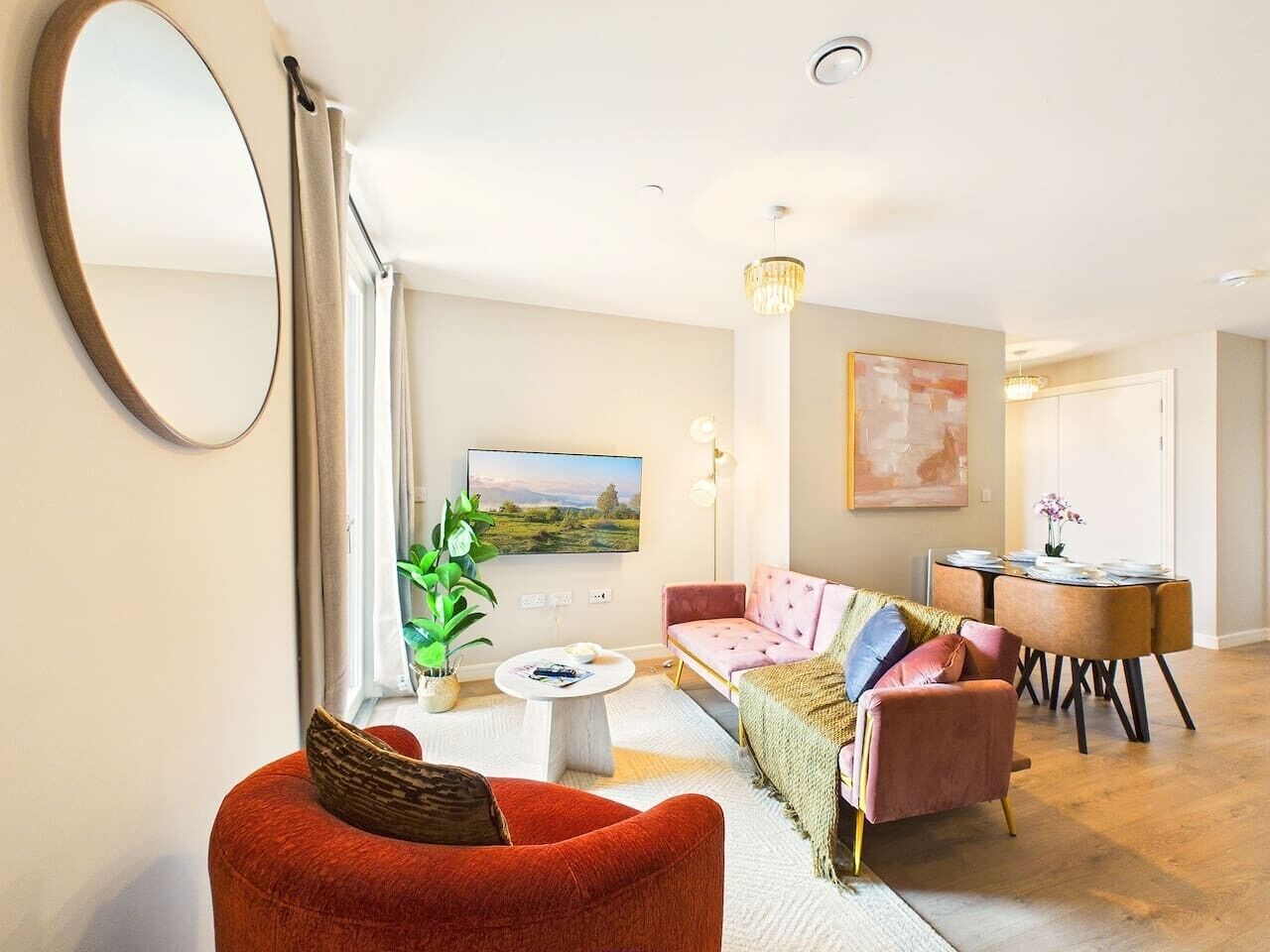 A living room with a sofa, a red chair, a coffee table, a TV, and a dining area with a table and chairs.