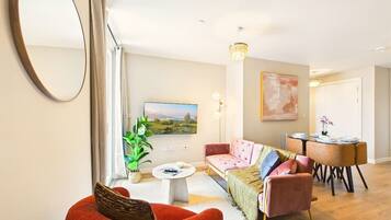 A living room with a sofa, a red chair, a coffee table, a TV, and a dining area with a table and chairs.