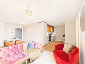 Ein modernes Wohnzimmer mit einem rosa Sofa, einem roten Sessel und einem Essbereich mit Tisch für zwei Personen.