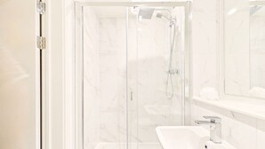 Un baño moderno con ducha envuelta en vidrio, un lavabo blanco y un espejo sobre el lavabo.