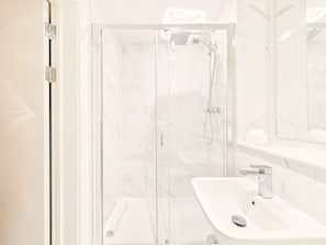 Ein modernes Badezimmer mit einer gläsernen Dusche, einem weißen Waschbecken und einem Spiegel darüber.