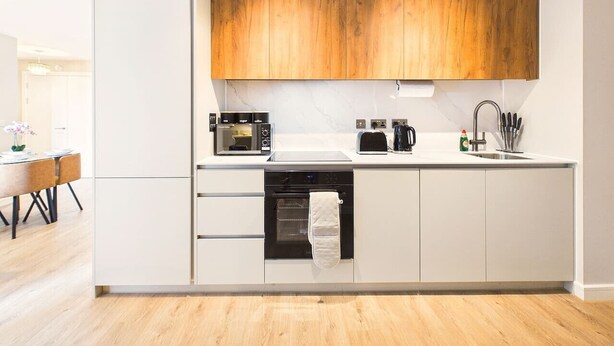 Una cocina moderna con armarios blancos, encimera de madera y horno empotrado.