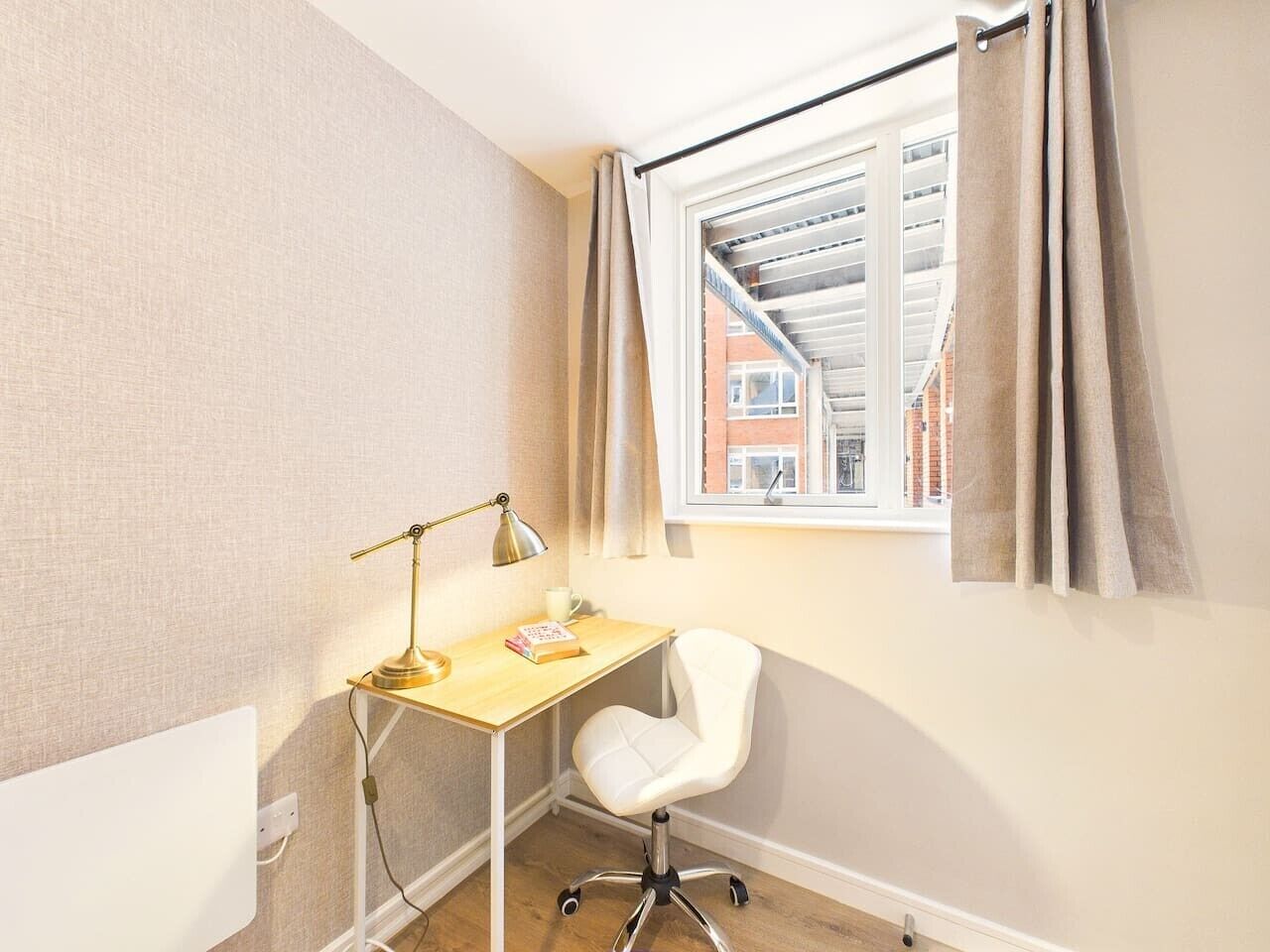 A small, well-lit room with a desk, chair, and a window with curtains.