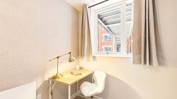 A small, well-lit room with a desk, chair, and a window with curtains.