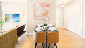 Un comedor con una mesa redonda dispuesta para cuatro, un cuadro en la pared y un pasillo que lleva a una puerta.