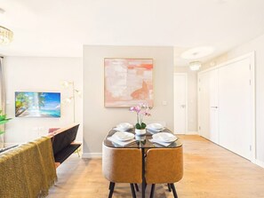 Ein Essbereich mit einem runden Tisch, gedeckt für vier Personen, einem Bild an der Wand und einem Gang zu einer Tür.