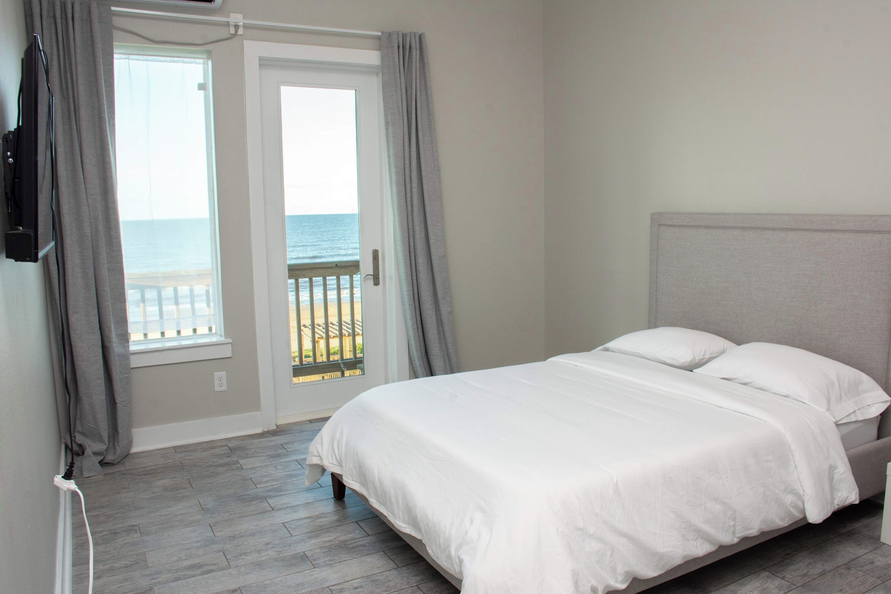 Ein Hotelzimmer mit Bett, Fernseher, Meerblick durch eine Tür und einem Balkon.