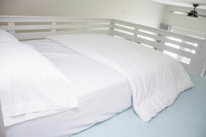 A bed with white bedding in a room with a white headboard and a ceiling fan. - Casa Dora Beach View Sunshine (Bolivar Peninsula)