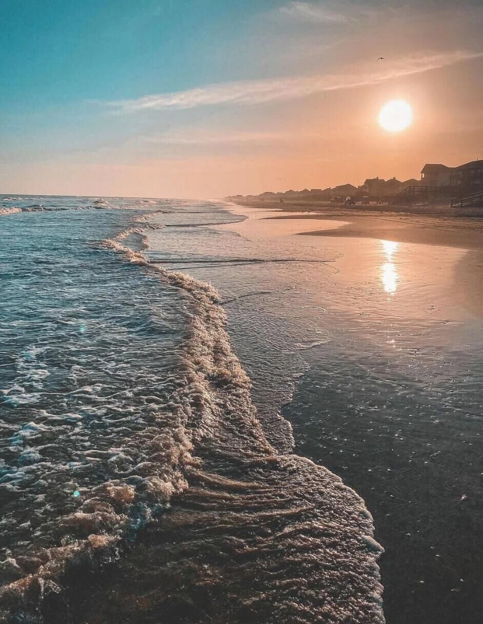 A beach scene with waves, a clear sky, and the sun setting or rising.