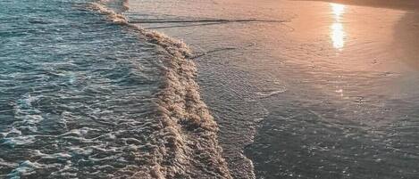 A beach scene with waves, a clear sky, and the sun setting or rising.