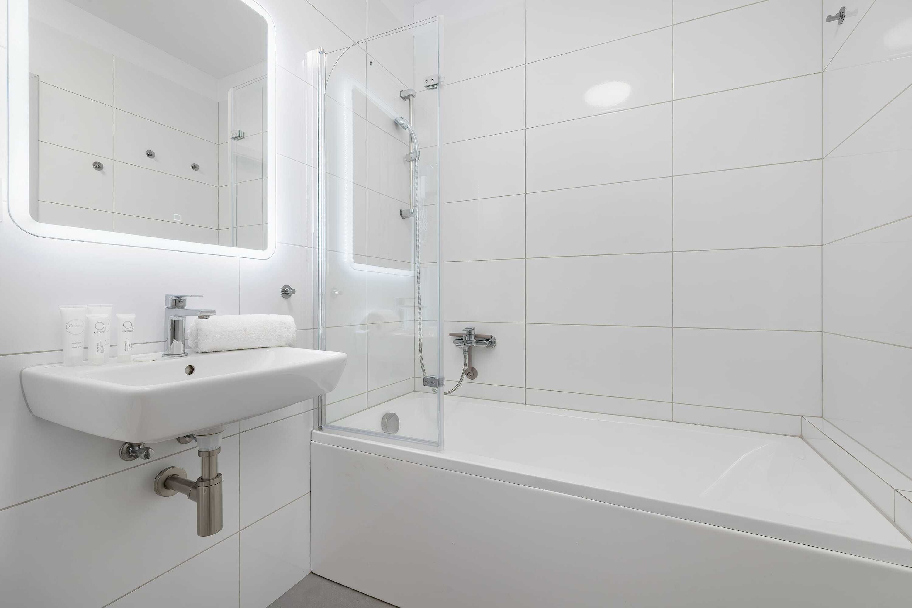 Et moderne badeværelse med en glasvæg omkring brusebadet, en hvid vask og et spejl over vasken.