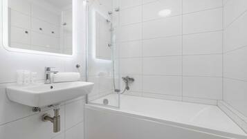Et moderne badeværelse med en glasvæg omkring brusebadet, en hvid vask og et spejl over vasken.