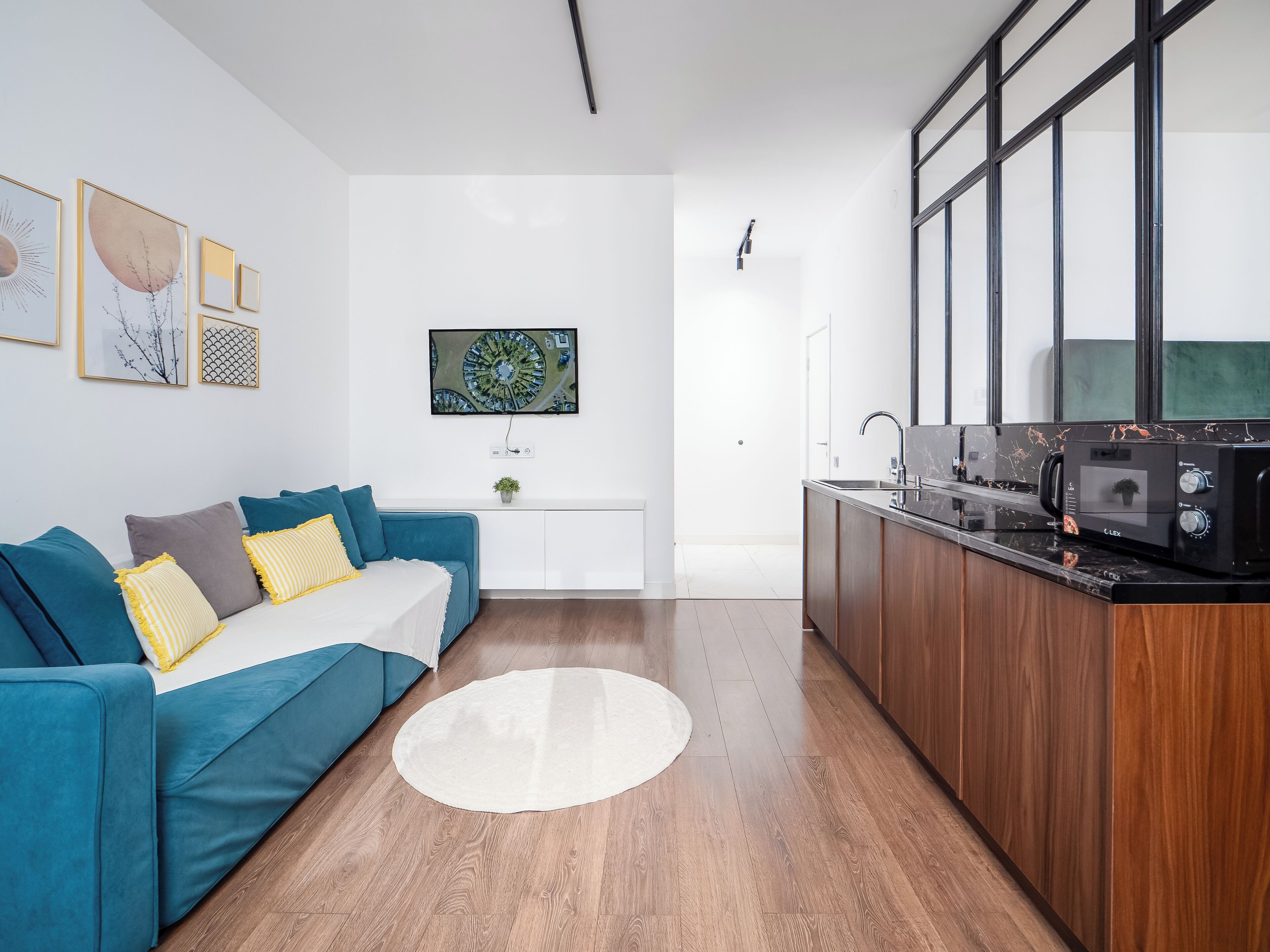 Uma sala de estar moderna com um sofá azul, um tapete branco e uma área de cozinha com micro-ondas e pia.
