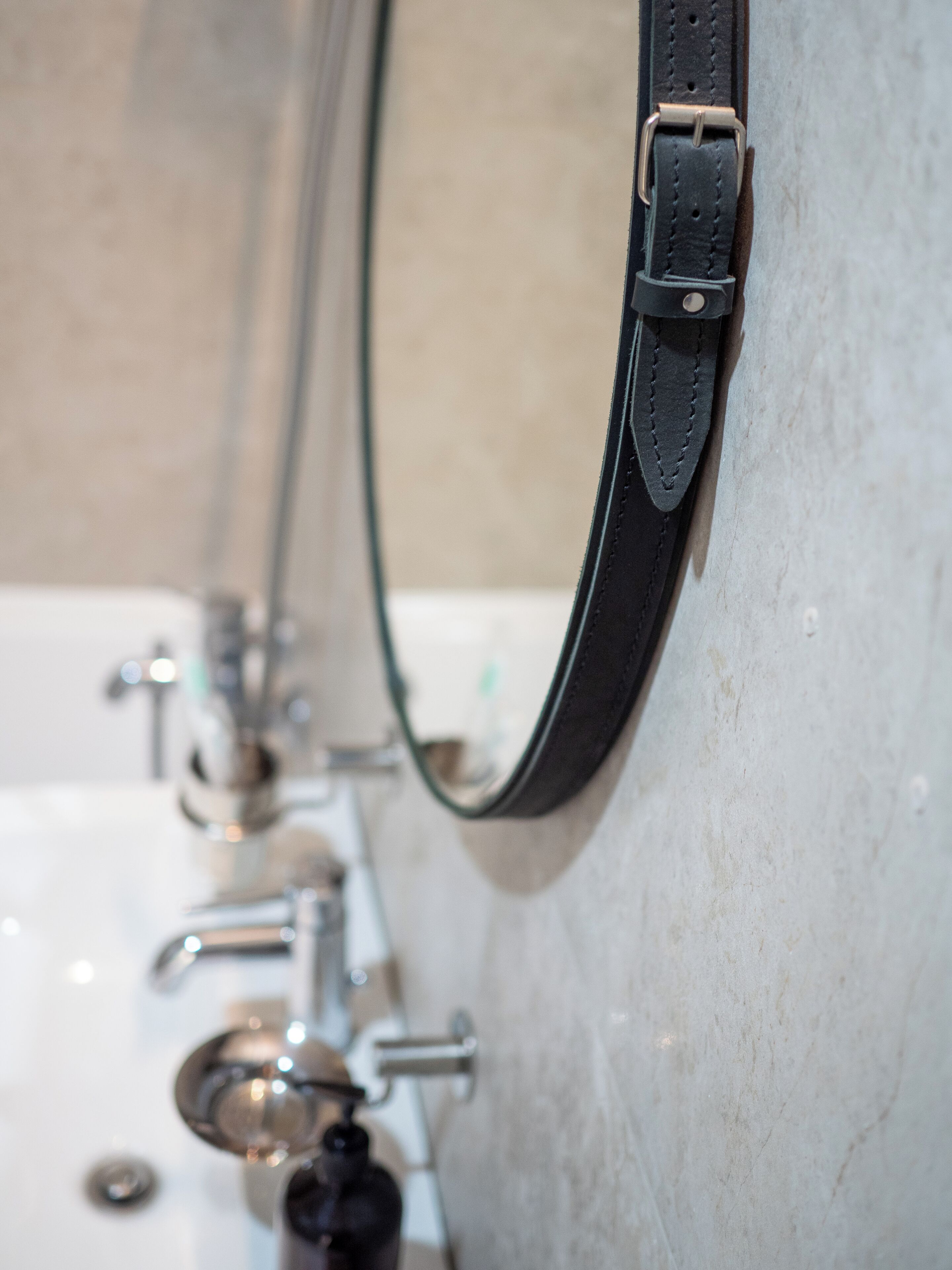 Un lavabo con grifo, un espejo y una correa negra colgada en la pared.
