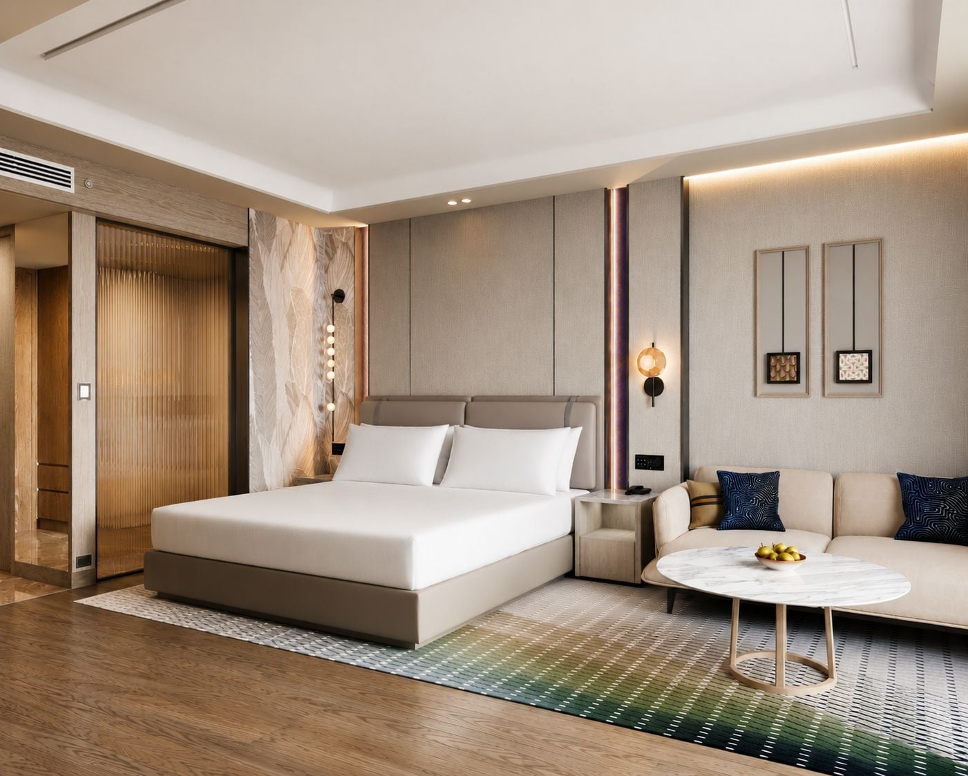 A modern hotel room with a large bed, a sofa, a round coffee table, and a wall-mounted light fixture.