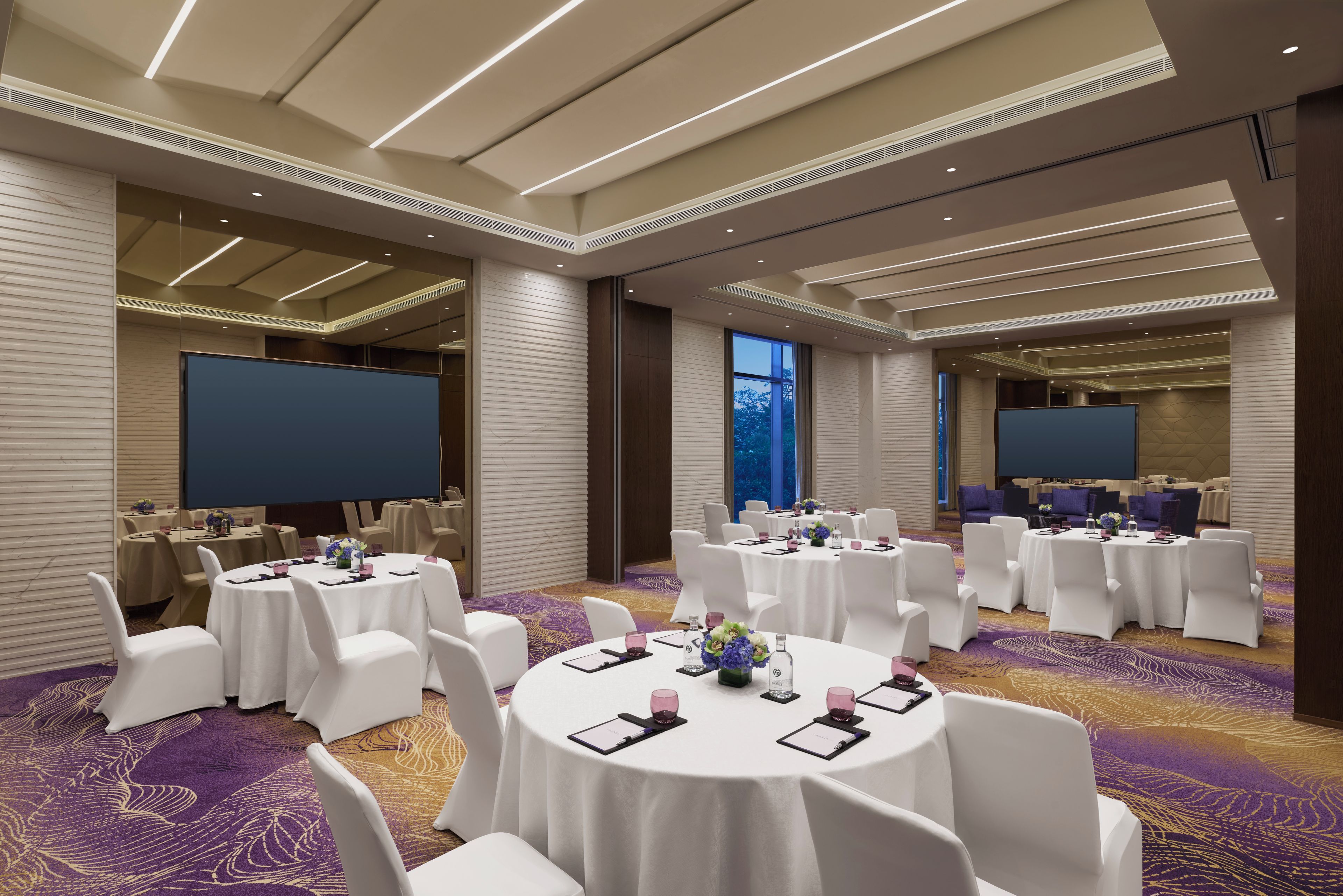 A conference room with round tables, white chairs, and a large screen.