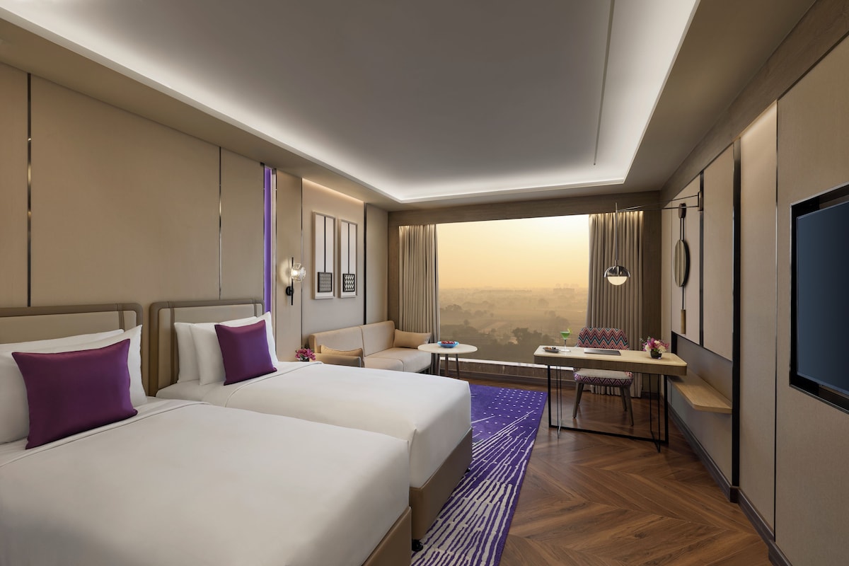 A hotel room with two beds, a dining table, and a view of the cityscape.