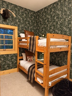 Habitación con literas, ventana, papel tapiz estampado y un peluche en la pared.