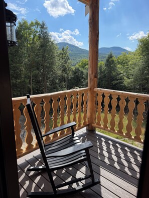 En træterrasse med bænk og gelænder, med udsigt over et skovklædt bjerglandskab.