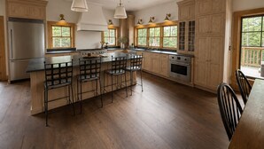 A spacious kitchen with wooden cabinets, a large island with bar stools, and pendant lighting. - Luxury Stowe Retreat Sleeps 18 Hot Tub & Mtn Views (Stowe)