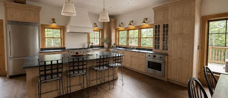 A spacious kitchen with wooden cabinets, a large island with bar stools, and pendant lighting.