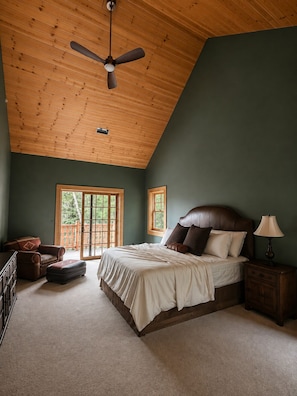 A bedroom with a sloped ceiling, a bed with a headboard, a nightstand, a chair, and a window with a view.