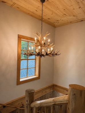 Ein Zimmer mit Holzbalkendecke, einer Kandelaber mit Geweih-Formen und einem Fenster mit Blick auf ein blaues Dach.
