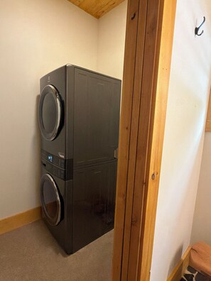 A compact, dark-colored laundry machine in a corner of a room with wooden trim and a white wall.