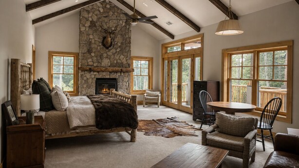 A spacious living room with a stone fireplace, wooden beams, a large window, and a cozy seating area.