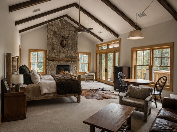 A spacious living room with a stone fireplace, wooden beams, a large window, and a cozy seating area.