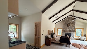 A spacious living room with a stone fireplace, wooden beams, a dining area, and a view of the outdoors.
