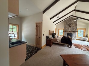 A spacious living room with a stone fireplace, wooden beams, a dining area, and a view of the outdoors.
