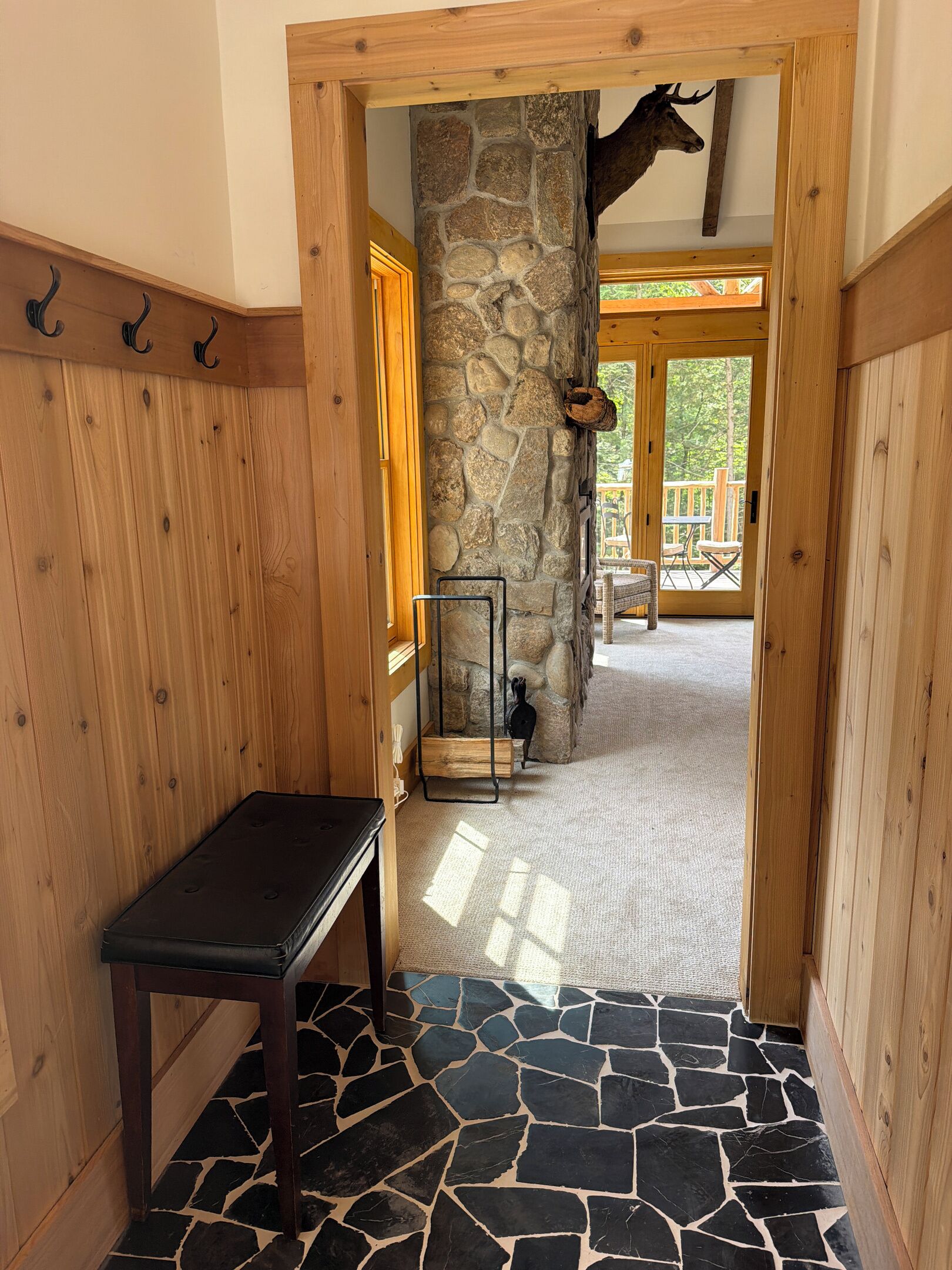 A hallway with a stone pillar, a wooden bench, and a view into a room with a wooden deck.