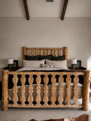 Una cama con cabecera y marco decorativos de madera. Hay dos mesitas de noche con lámparas.