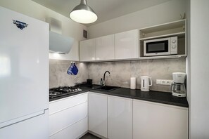 A modern kitchen with white cabinets, a black countertop, a built-in microwave, a Bosch coffee maker, and a Beko kettle. - RentPlanet - Apartament Kołłątaja (Wrocław)