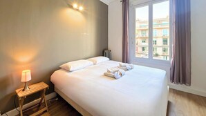 Una camera d'albergo con un letto, un comodino con una lampada e una finestra con tende.