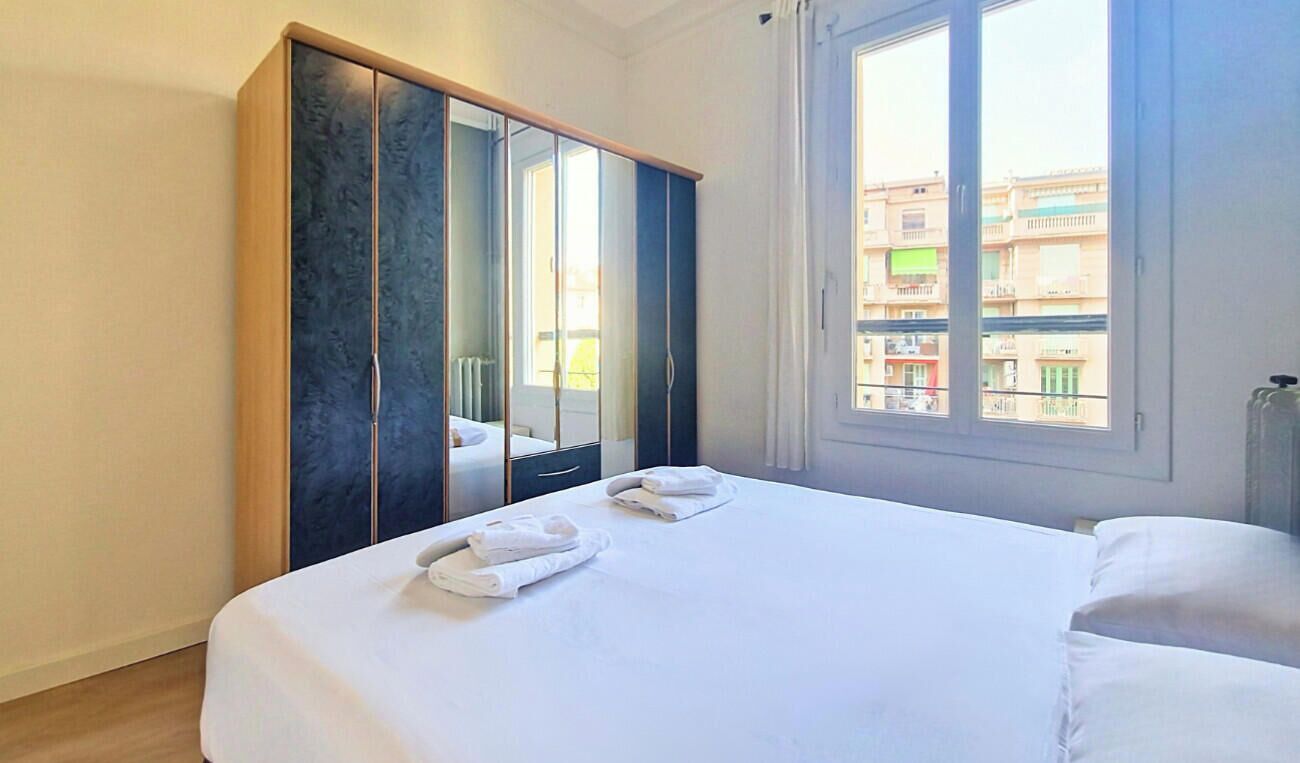 Une chambre d’hôtel avec un lit, une armoire et une fenêtre donnant sur des immeubles.