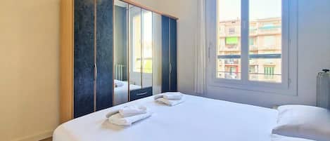 A hotel room with a bed, a wardrobe, and a window with a view of buildings.