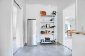 Una cucina moderna con frigorifero in acciaio inossidabile, scaffali aperti con diversi oggetti da cucina e vista su un'area relax all'aperto.