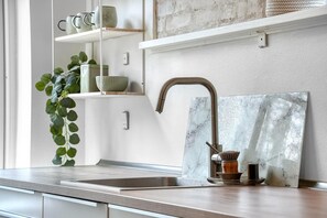 A kitchen with a stainless steel sink, a marble backsplash, and a plant on the left.