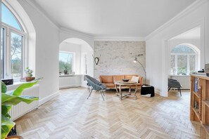 A spacious room with a herringbone wooden floor, a leather sofa, a round coffee table, and a black chair.