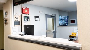 Zona de recepción con un mostrador, una computadora, un dispositivo StarLink, un letrero de WiFi, un aviso de cargo por mascotas y un letrero de prohibido fumar.