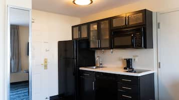Cocina compacta con muebles oscuros, un refrigerador negro, microondas y cafetera.