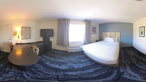 Habitación de hotel con cama, escritorio, televisión y ventana con cortinas.