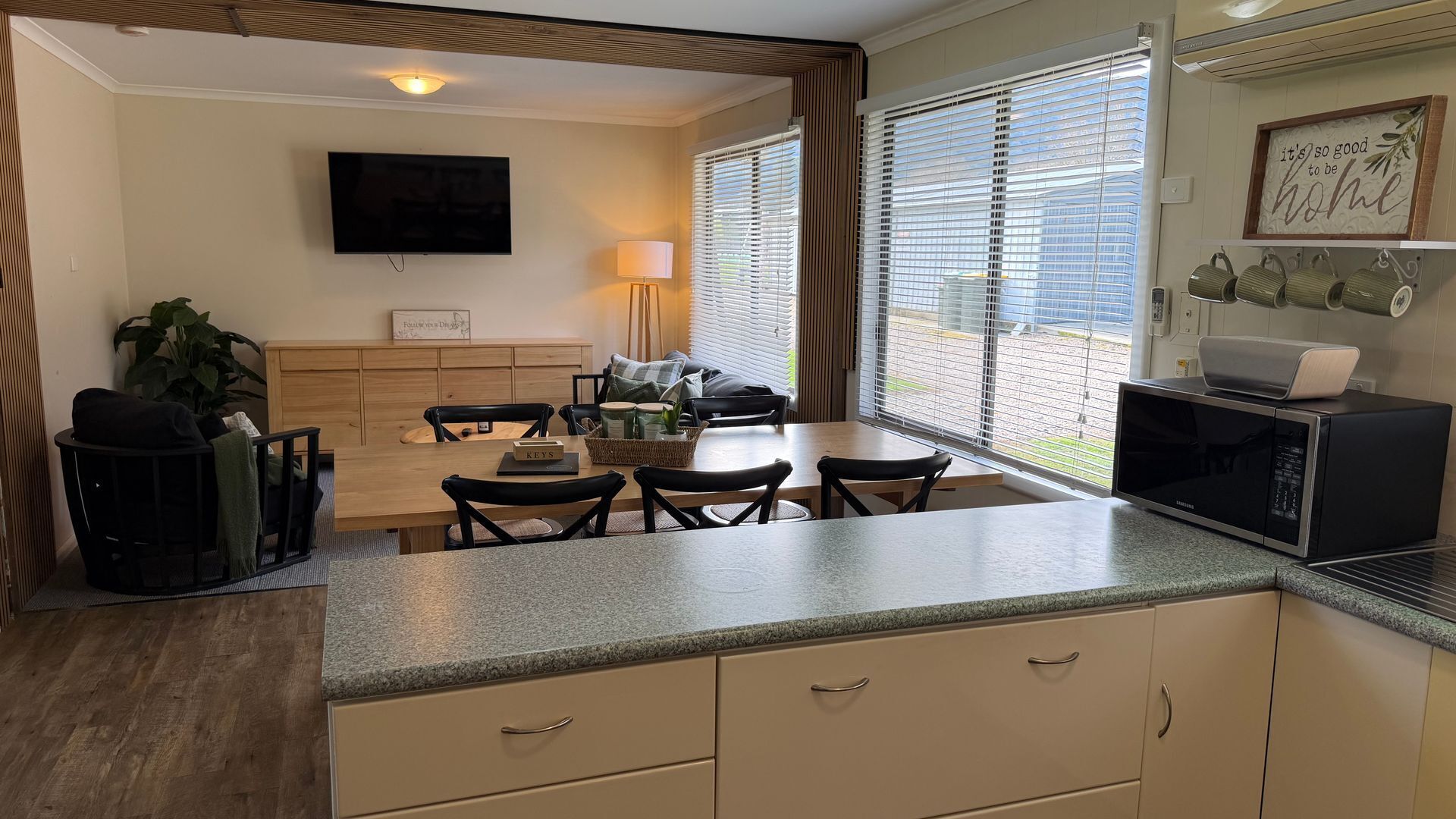 A compact kitchen with a dining area, a flat-screen TV, and a window with blinds.