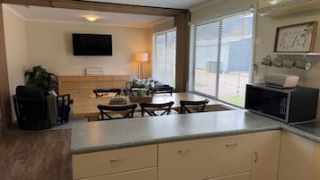 A compact kitchen with a dining area, a flat-screen TV, and a window with blinds.